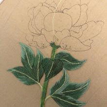a hand-drawn outline of a peony on beige silk with the stem and leaves embroidered in green