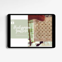A tablet showing an image of two fingers holding up a sashiko stitched coaster in front of a sunny window and a title card that says "video course Hydrangea pattern by sashiko.lab"
