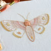An anatomical Moth embroidered with lots of depth and texture in pinks and yellows on white fabric