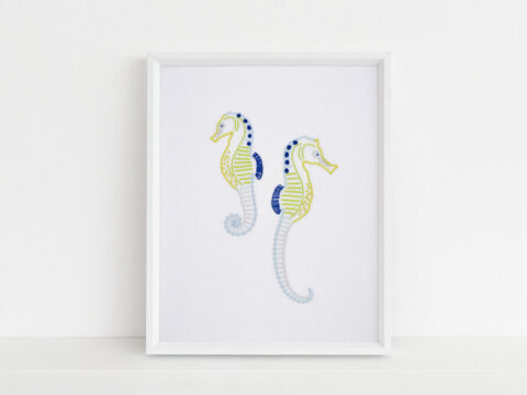 Anatomical Seahorses embroidery in blues and yellows on white fabric in a white frame