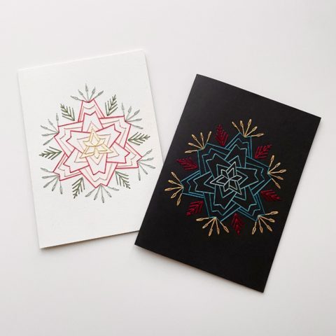 A star-shaped flower in blue, raspberry, and yellow, stitched on white and black greeting cards