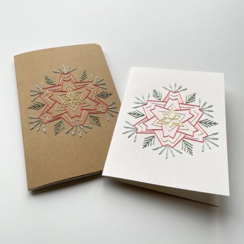 A star-shaped flower in blue, raspberry, and yellow, stitched on a kraft brown notebook cover and a white greeting card