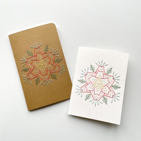 A star-shaped flower in blue, raspberry, and yellow, stitched on a kraft brown notebook cover and a white greeting card