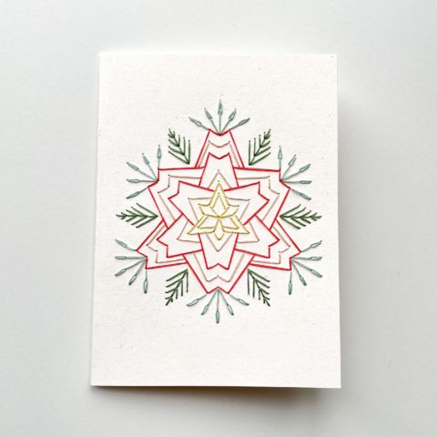 A star-shaped flower in blue, raspberry, and yellow, stitched on a white greeting card