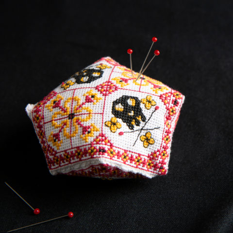 A biscornu style pincushion featuring folk art skulls in black and geometric folk art borders in red