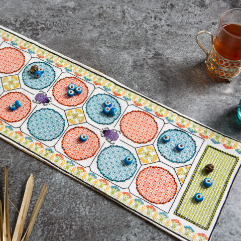 A cross-stitched mancala board with beads on top
