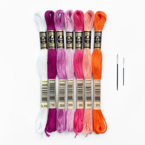 a bundle of embroidery floss in purples and oranges with two black and white needles on a white background