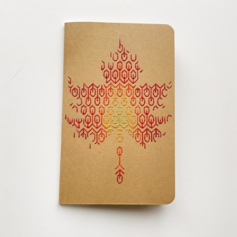A blackwork leaf design in fall colors embroidered onto a kraft brown notebook cover