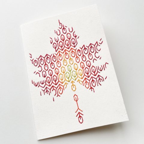 A blackwork leaf design in fall colors embroidered onto a white greeting card