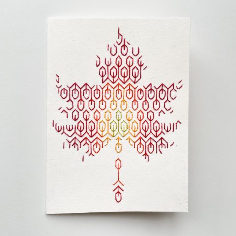 A blackwork leaf design in fall colors embroidered onto a white greeting card