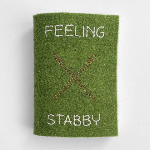 A small felt book in green with an image of a needle and the words "feeling stabby" embroidered on the front