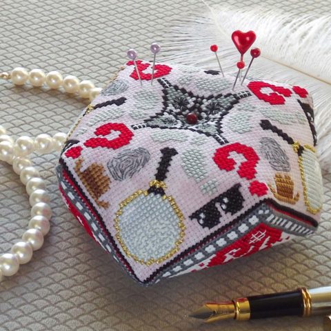 a cross-stitch biscornu pin cushion showing detective symbols like magnifying glasses and footprints