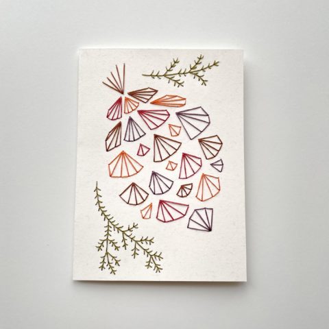 A geometric pinecone design in fall colors embroidered onto a white greeting card