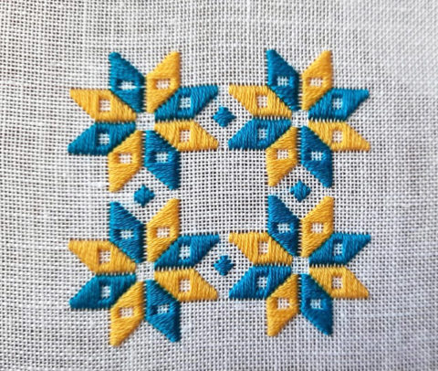 A set of four stars made of 8 alternating blue and yellow diamonds stitched in a square pattern on white linen