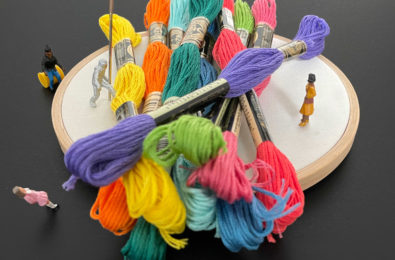 Tiny people standing, sitting, and climbing around a giant pile of embroidery supplies