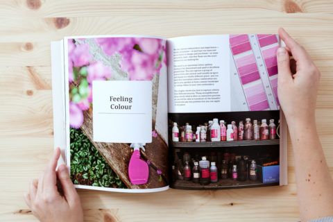 A spread of two pages in a book. The left page shows the title "feeling colour" and the right page shows a collage of images of various fuchsia images including flowers, paint chips, and bottles of ink