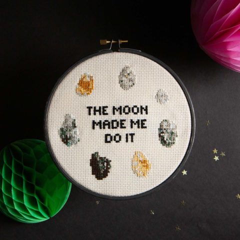 Cross-stitch of seven small rocks surrounding the words "The Moon Made Me Do It"