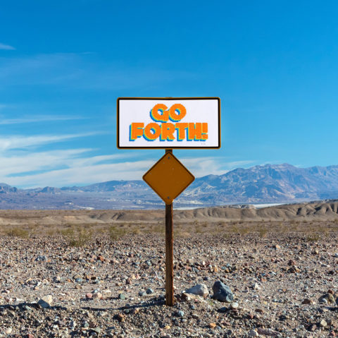 White sign with the words "Go Forth" in orange capital letters out in a desert landscape