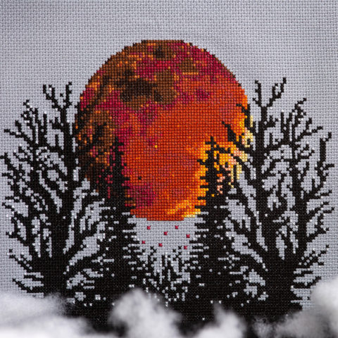 Cross stitch of a blood red moon behind black skeletal trees