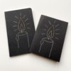 A drawing of a candle flame stitched on a black greeting card and notebook