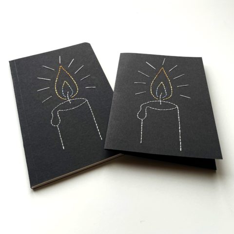 A drawing of a candle flame stitched on a black greeting card and notebook