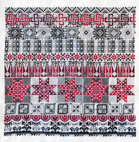 Rows of traditional Palestinian tatreez cross-stitch motifs stitched in red and gray on white fabric