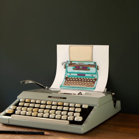 A light green grey typewriter where the inserted page is a cross-stitch of a seagreen typewriter with a blank page