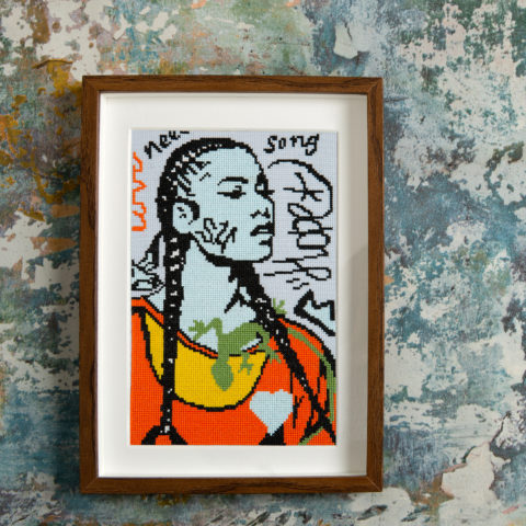 Cross stitch of a drawing of a young Black woman with two long braids and a bright orange sweater overlaid with graffiti writing, a heart, and a green lizard