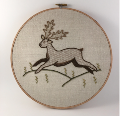 Old-fashioned embroidery of a stag leaping over grassy hills
