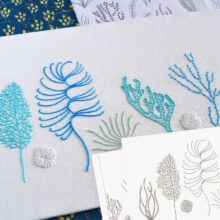 Various corals embroidered in blue and white shown with a corner of the printed embroidery pattern