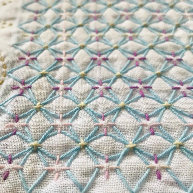 A close-up of ajisai-sashi hydrangea sashiko stitches done in light blue, purple, and yellow on white fabric