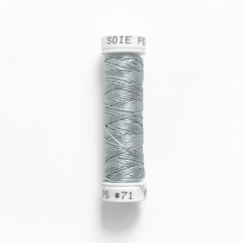 a spool of au ver a soie perlee 071 light grey silk thread on a white background