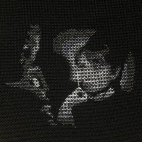 audrey hepburn's face illuminated by a man holding up a match stitched in grayscale on black fabric