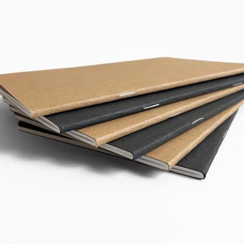 The spines of 6 black and kraft brown notebooks stacked in a fan