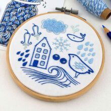 Several folk art objects embroidered in blue in a wooden hoop