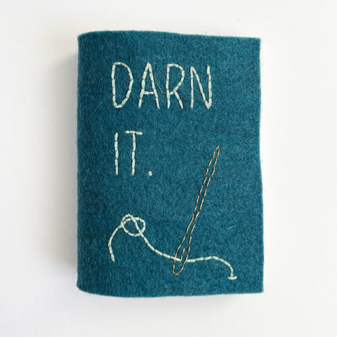 A small felt book in turquoise with an image of a needle and the words "darn it" embroidered on the front