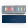 Sashiko thread bobbins in 29 colors arranged in a rainbow inside the bottom of a blue paper gift box. Laid on top is a sheet of vellum with the word "sashiko" and a contents list in Japanese. Displayed below is the lid of the box, which has the word "sashiko" stamped in white.
