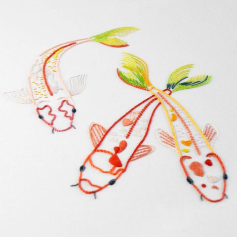 three embroidered red koi fish with green tails on white fabric
