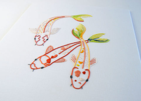 three embroidered red koi fish with green tails on white fabric