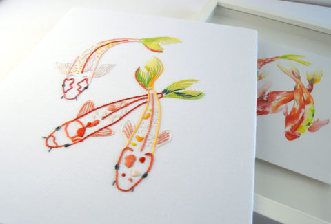 three embroidered red koi fish with green tails on white fabric in front of a matching watercolor painting