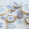 Snowflakes of various types and sizes embroidered in blue on white fabric, some displayed in small wooden hoops