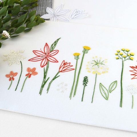a row of all different yellow and red wild flowers with green leaves embroidered on white fabric