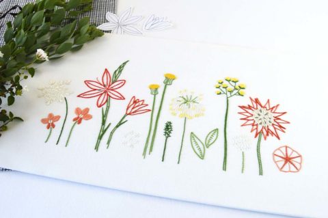 a row of all different yellow and red wild flowers with green leaves embroidered on white fabric