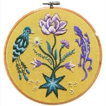 blue and purple flowers and garden animals embroidered on yellow fabric in a hoop