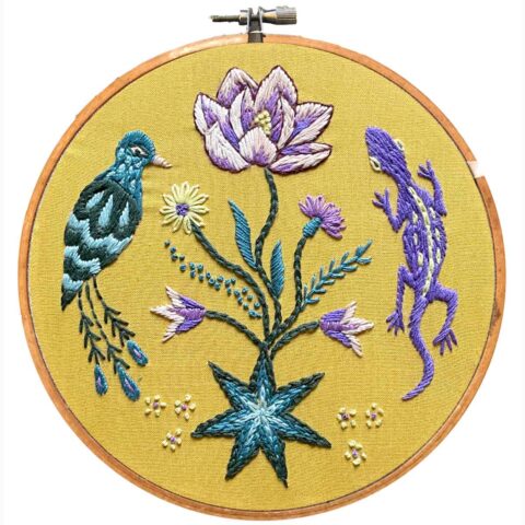 blue and purple flowers and garden animals embroidered on yellow fabric in a hoop