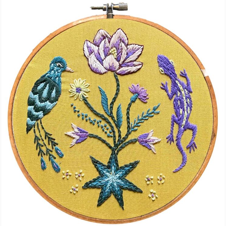 blue and purple flowers and garden animals embroidered on yellow fabric in a hoop