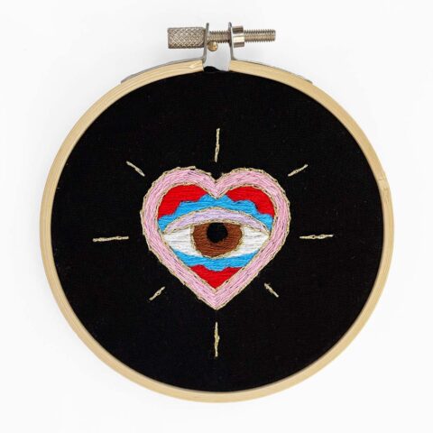 a skeptical-looking eye inside a heart, embroidered on black fabric