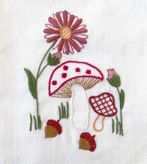 mushrooms, flowers, and acorns embroidered on a white linen tea towel