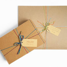two gifts wrapped in brown carboard with colorful string and gift tags