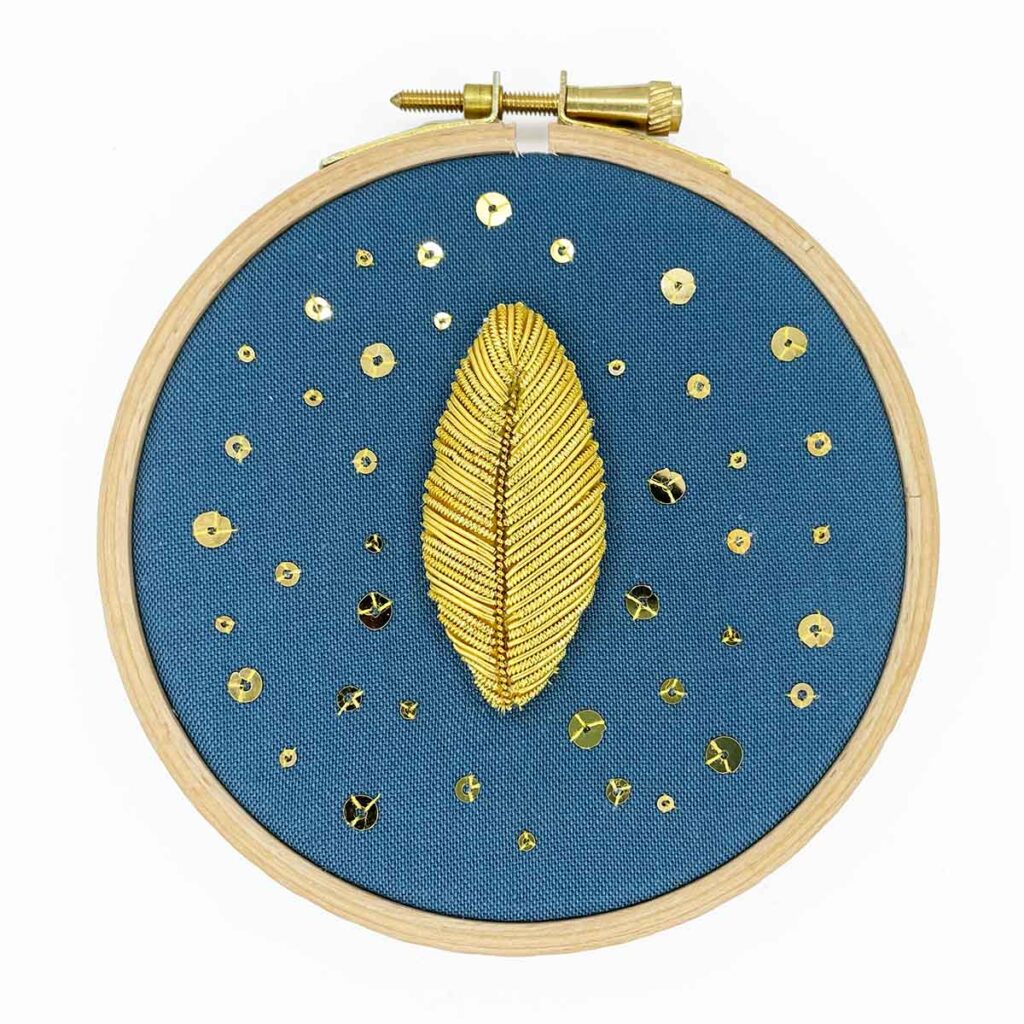 goldwork embroidery leaf with spangles on blue fabric in a wooden hoop